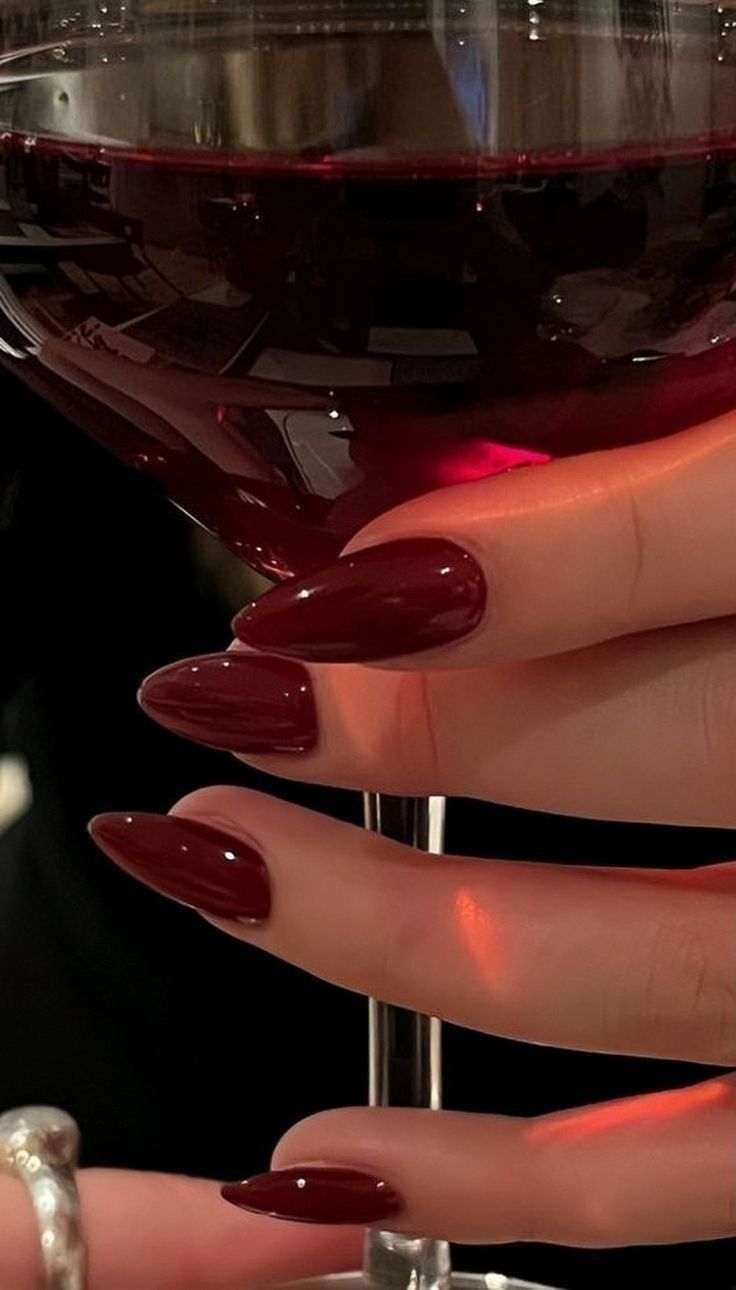 Hand with dark red nails holding a glass of red wine