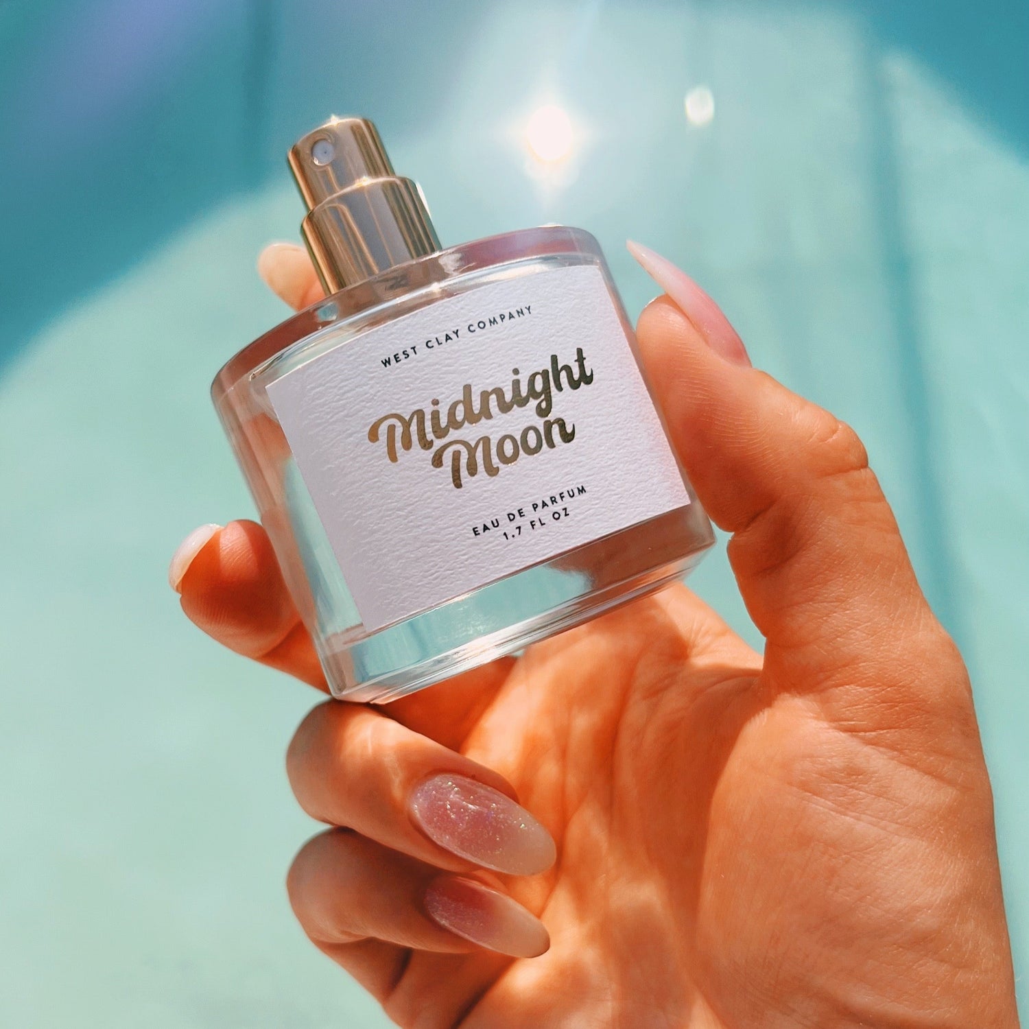 Hand holding a perfume bottle labeled 'Midnight Moon' against a light blue background