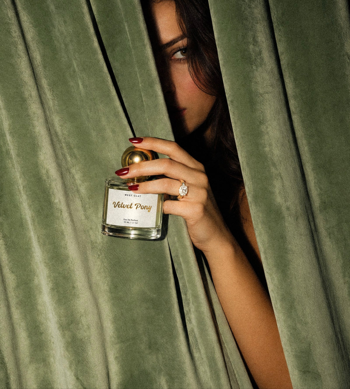 Velvet Pony perfume held beside deep green curtains